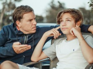 A father tries to talk to his son, who rolls his eyes and blocks his ears.