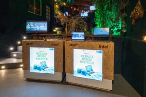 Sustainable laptop display featuring Acer and Intel devices with screens reading "Reduce Reuse Recycle" at an event showcase.